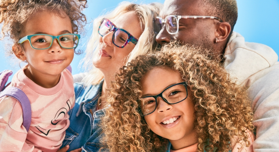 Four people wearing glasses, smiling brightly. Glasses have colorful frames: green, purple, and white.