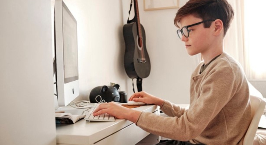 Boy using a desktop computer with a keyboard and mouse on a white desk.