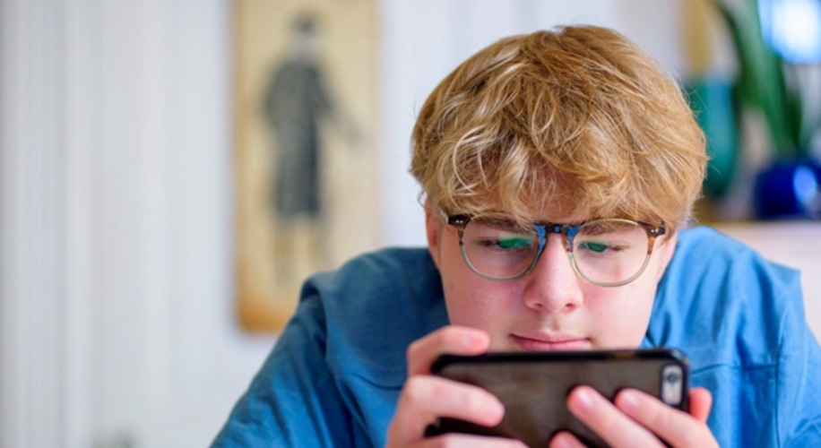 Teen wearing glasses using a smartphone.
