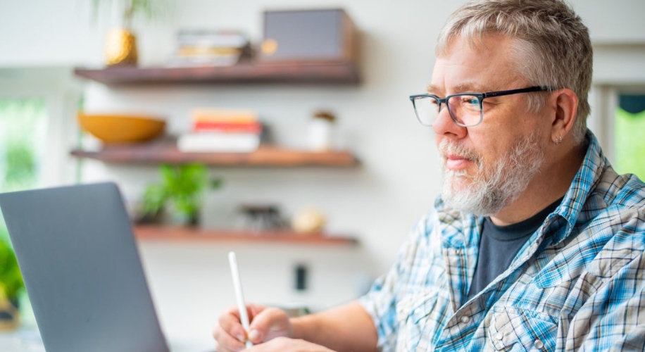 Person using a stylus and laptop wearing glasses and a plaid shirt.