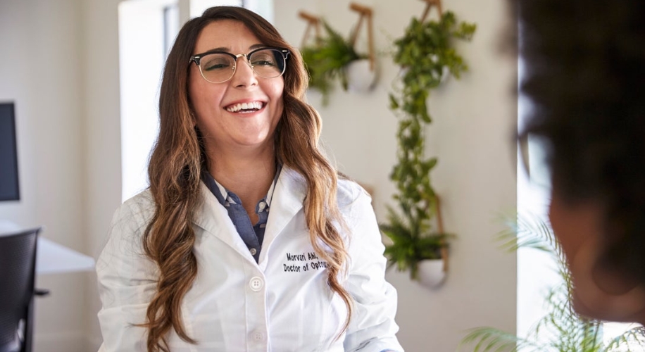 Doctor wearing a white lab coat and glasses, with &quot;Morvarid Abbey, Doctor of Optometry&quot; embroidered on the coat.