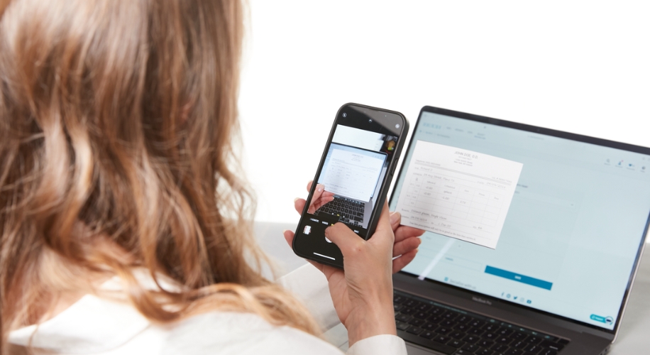 Person scans document with smartphone in front of a laptop. Document shows &quot;Patient Jane Doe 1/1/10.&quot;