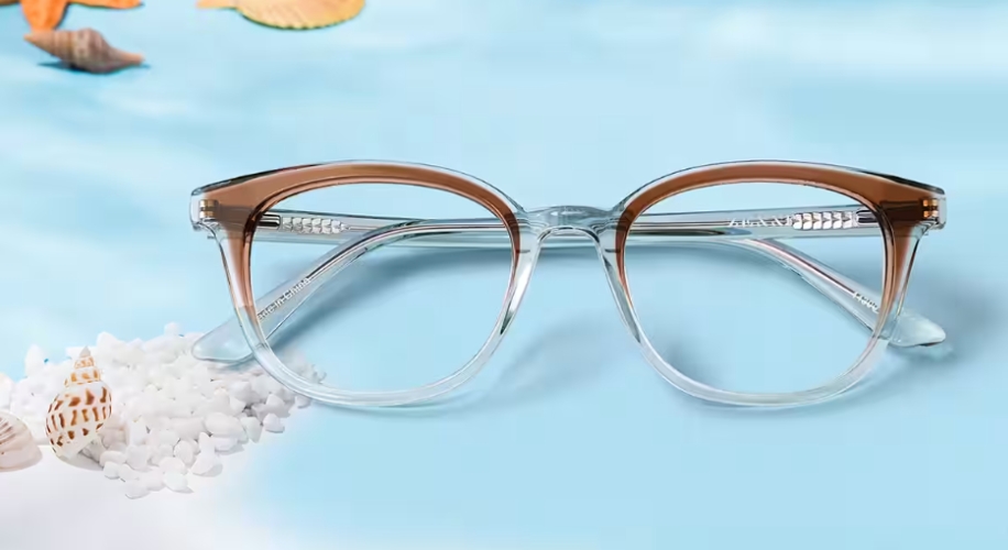 Clear frame eyeglasses with brown accents and transparent lenses, placed on a blue surface with white granules.