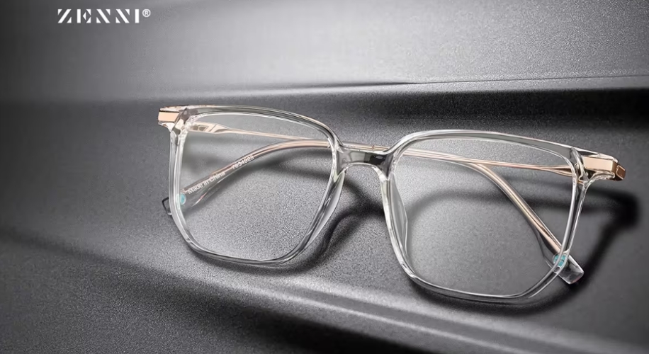 Zenni transparent square eyeglasses with light metal temples on a gray surface, Zenni logo in top left.