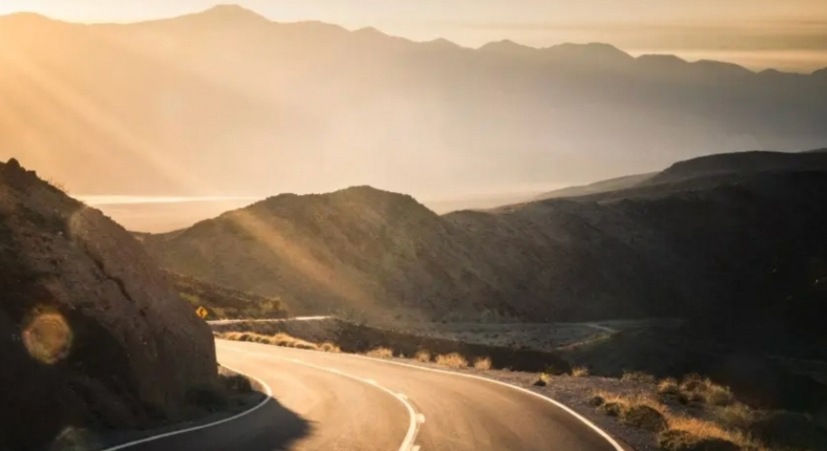 Winding road through mountainous landscape with sunlight streaming over the hills.