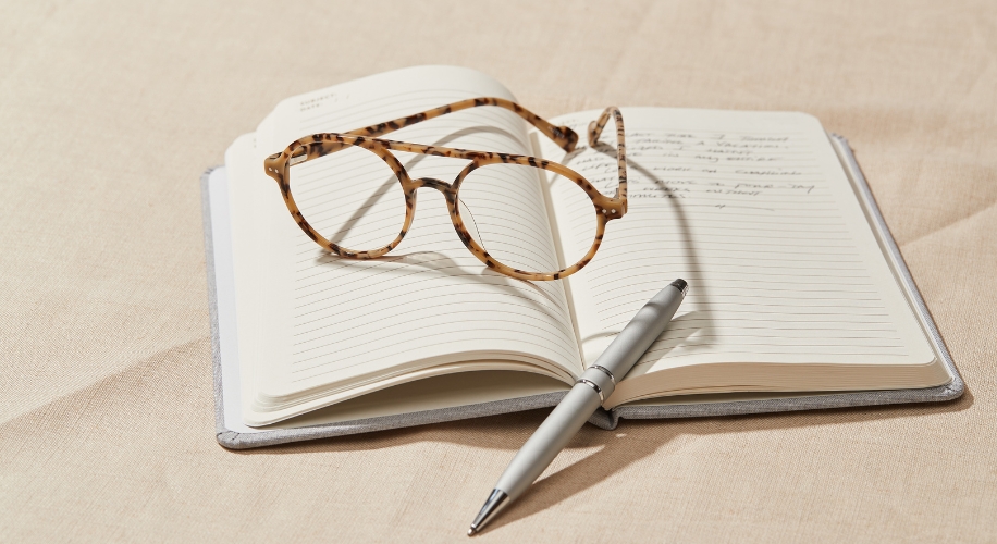 Open notebook with handwritten notes, tortoiseshell glasses, and a silver pen resting on its pages.