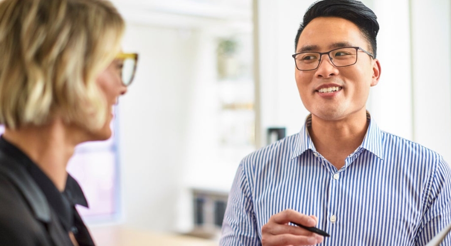 Man in striped shirt and glasses holding a pen, engaged in conversation with a blonde woman.