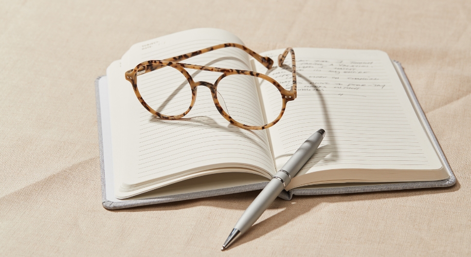 Eyeglasses and pen placed on an open notebook with lined pages.