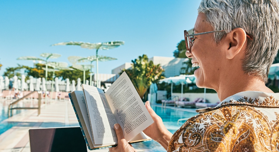 Person holding an open book while smiling, poolside.