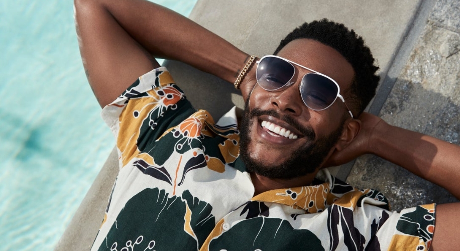 Man wearing sunglasses and a floral print shirt, smiling and relaxing near a pool.
