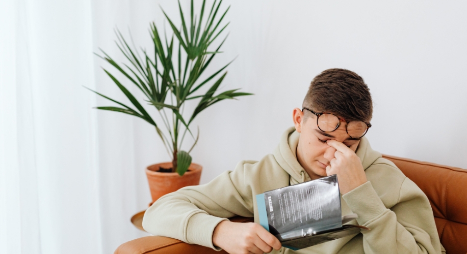 Man reading a book, wearing glasses on his forehead and rubbing his eyes.