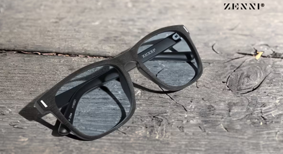 Zenni black-framed sunglasses with dark lenses, placed on a wooden surface. Twill in Charcoal. Label: 7350211.