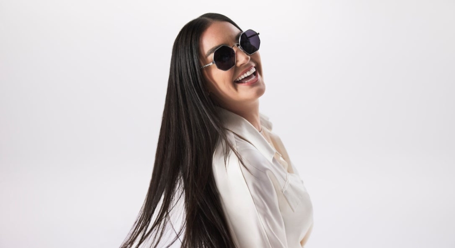 Woman wearing large, round black sunglasses, smiling and looking to the side.