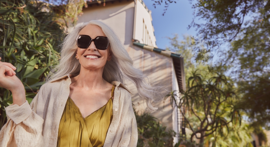 Woman with long, gray hair wearing black sunglasses, a green top, and a cream-colored shirt.