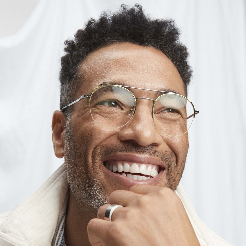 Man wearing clear round eyeglasses, smiling, and resting his chin on his hand.