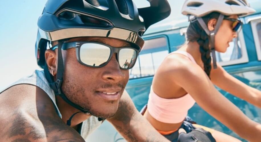 Man and woman wearing cycling helmets and sunglasses riding bicycles.