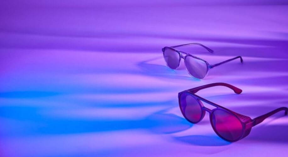 Two pairs of sunglasses on a purple and blue lit surface.