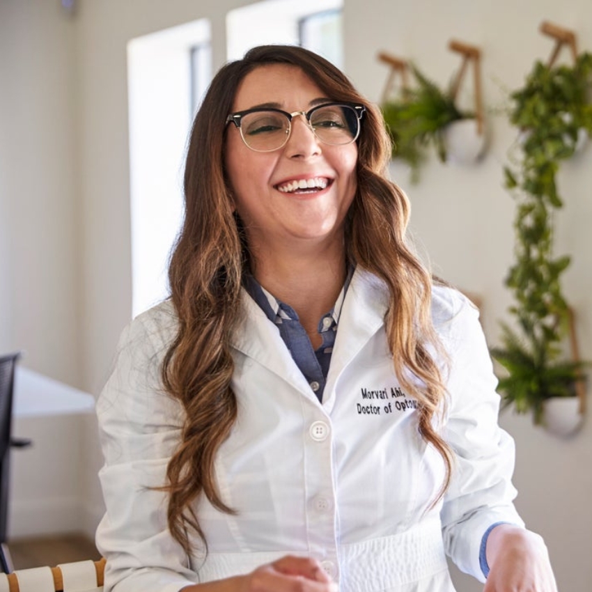 Doctor wearing glasses and a white lab coat that reads, "Morvari Ahi, Doctor of Optometry" on the left side.