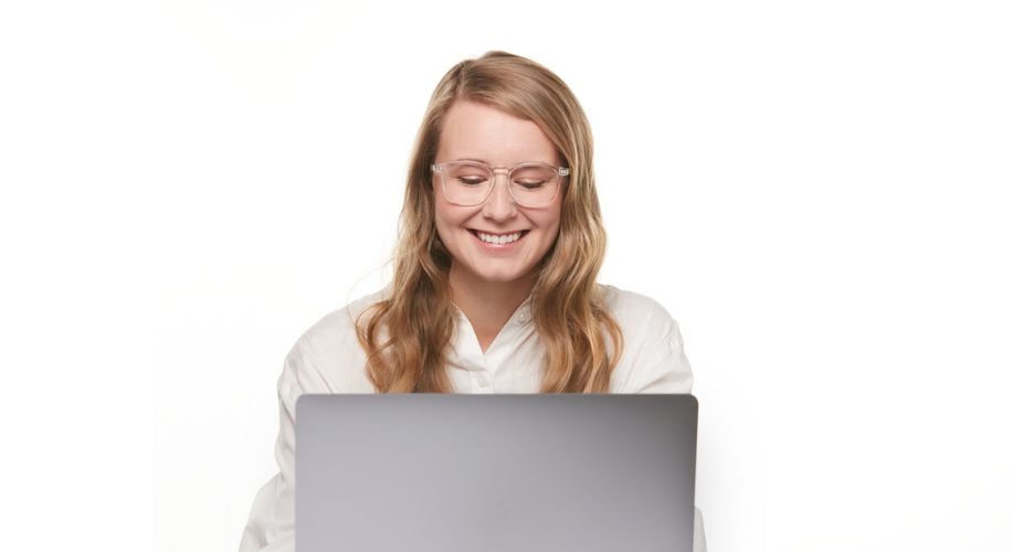 Person wearing glasses, sitting in front of an open laptop, smiling.