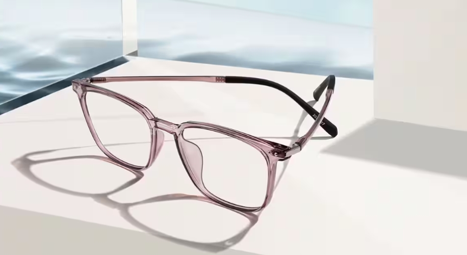 Transparent pink eyeglasses with black temples placed on a white surface.