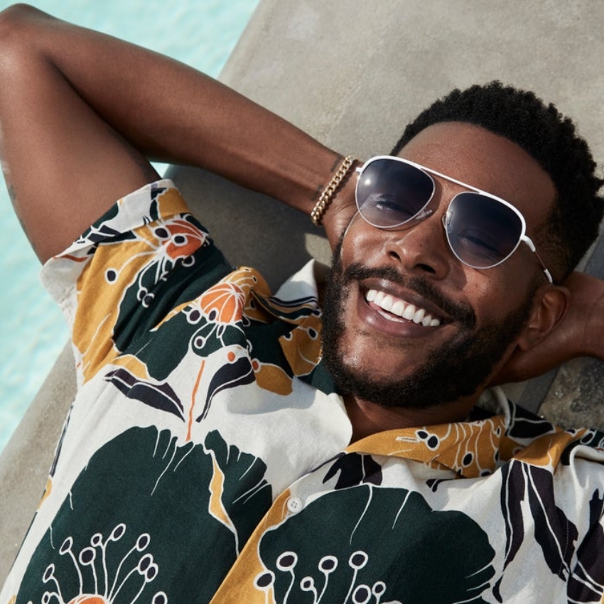Man in floral shirt and sunglasses, smiling and relaxing.