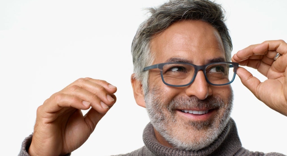 Man adjusting stylish, rectangular eyeglasses, wearing a grey turtleneck sweater.