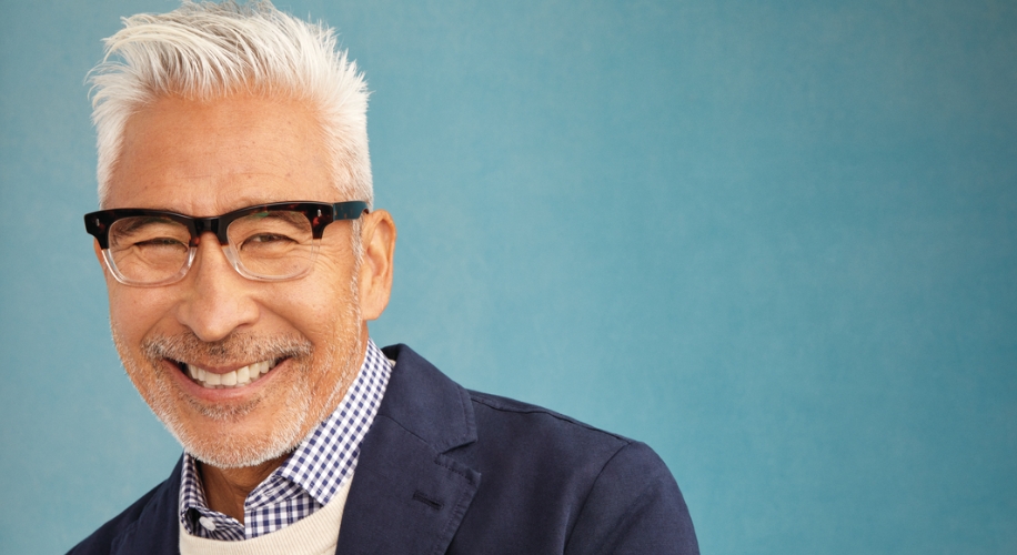 Man wearing black rectangular glasses, a blue checkered shirt, and a navy blazer with a white sweater