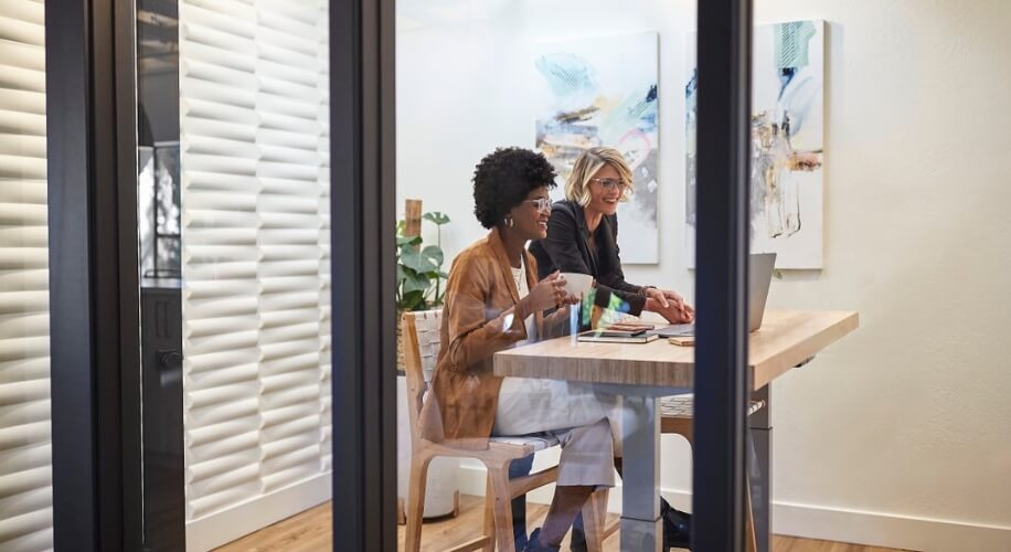 Two people sitting at a desk, collaborating over a laptop in a modern office space.
