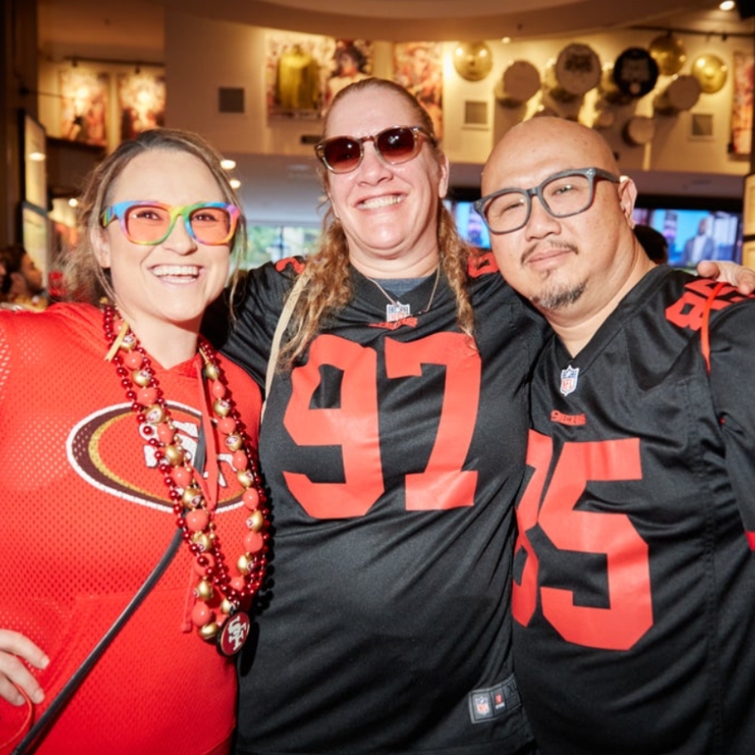 Group of three people wearing San Francisco 49ers jerseys, numbers 97 and 85, and a beaded necklace.