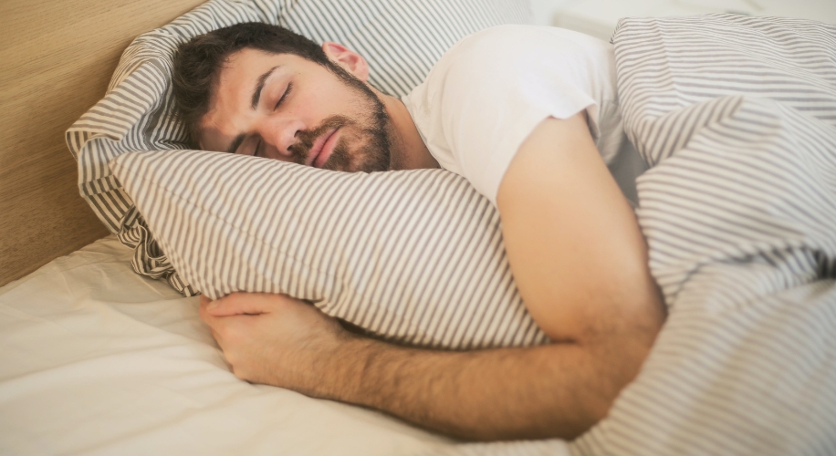 Man sleeping in bed with striped sheets and pillowcases.