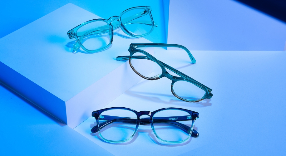 Three pairs of eyeglasses in different shades of blue displayed on angular white surfaces.