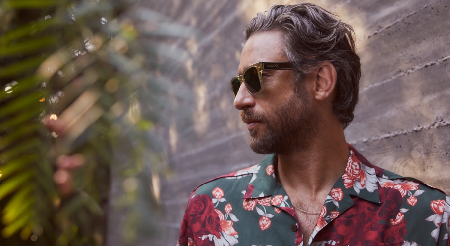 Man wearing a floral shirt and black sunglasses with &quot;WOOD&quot; inscription on the temples.