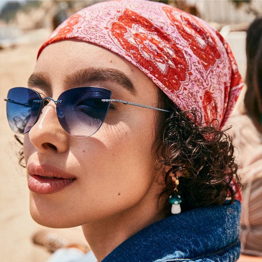 Woman wearing blue gradient sunglasses, a pink and red headscarf, and a blue denim top.