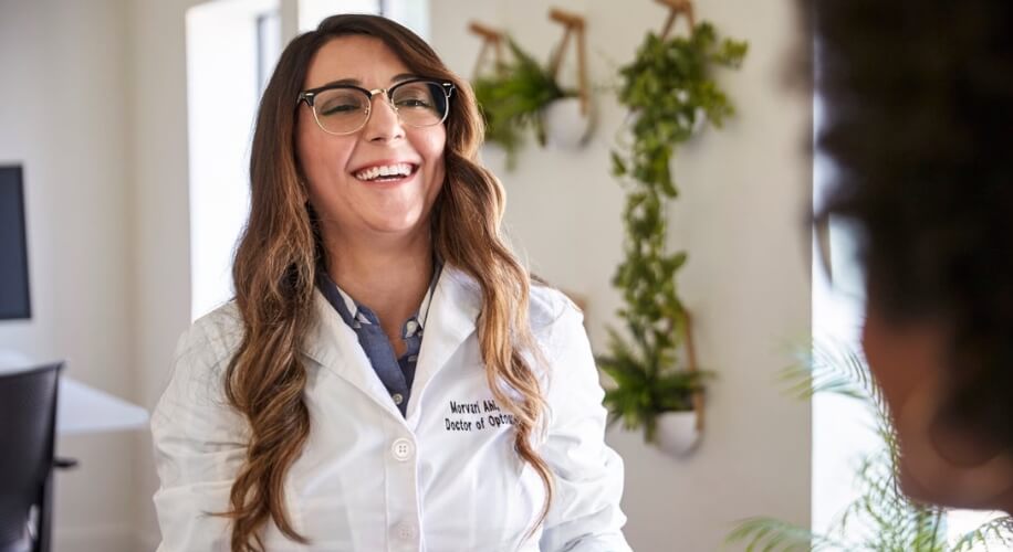 Optometrist smiling, wearing a white coat with the text &quot;Maryam Ahdout, Doctor of Optometry&quot;.