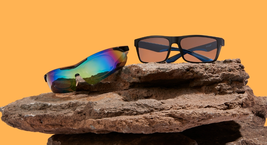 Two pairs of sunglasses on a rock; one with rainbow lenses and the other with brown lenses in black frames.
