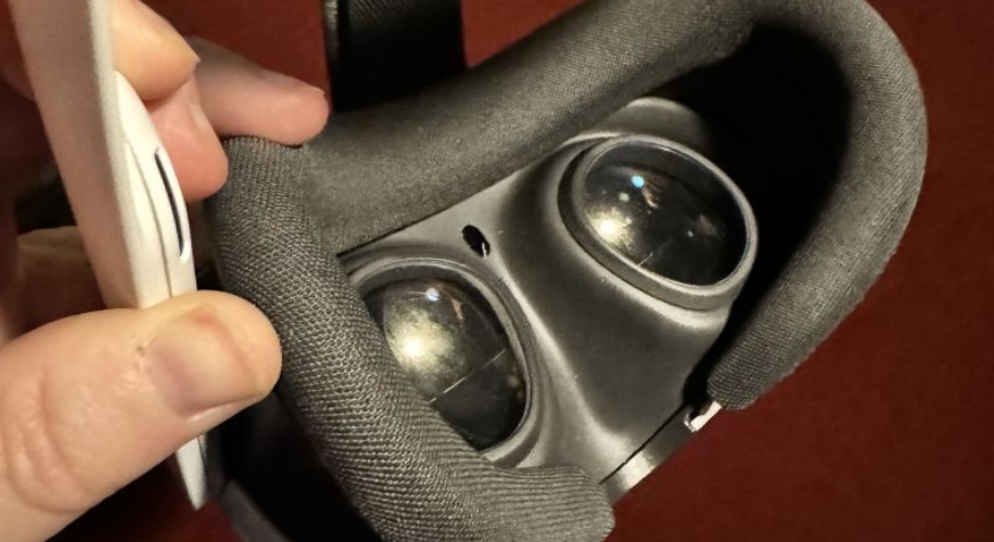 Virtual reality headset with thick padding and two visible lenses. Hand holding a white remote control.