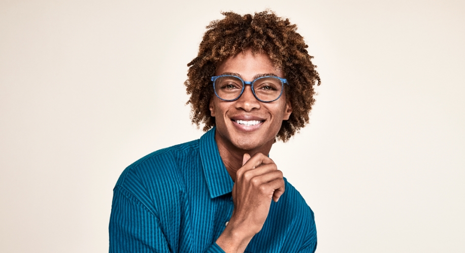 Man smiling and wearing blue-rimmed eyeglasses with a matching blue, striped shirt.