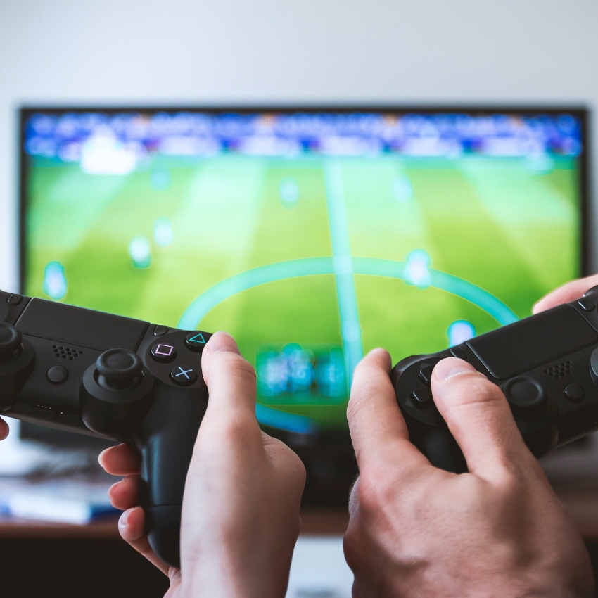 Two people holding black game controllers playing a soccer video game on a television.