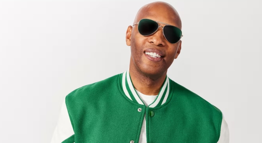 Man wearing aviator sunglasses and a green varsity jacket with a white shirt underneath.