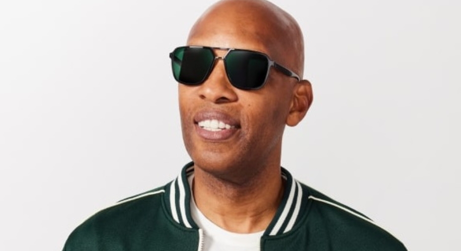 Man wearing dark sunglasses and a green jacket with white trim.