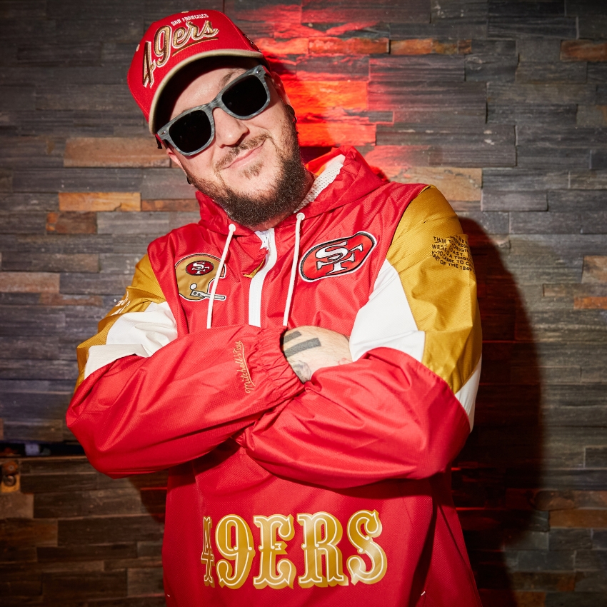 Person wearing San Francisco 49ers jacket and hat with "49ERS" in large gold letters on the jacket.