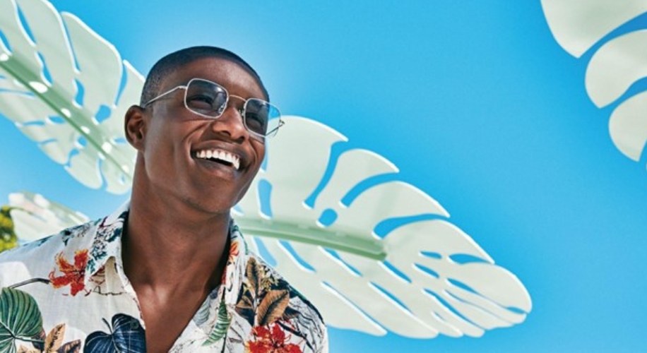 Man wearing reflective sunglasses and a floral shirt, smiling.