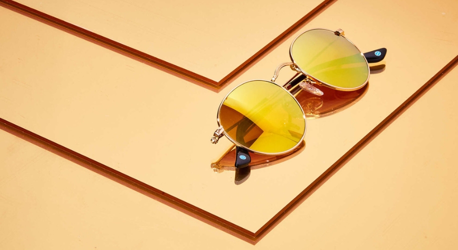 Sunglasses with round yellow-tinted lenses and dark black arms on a mirrored orange surface.
