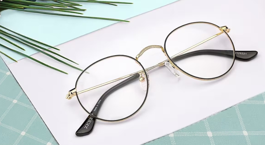 Gold-rimmed round eyeglasses with black temples on a light blue and white background.