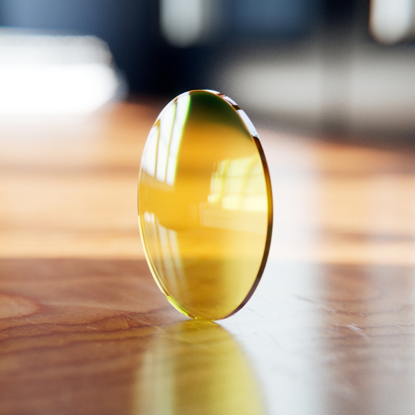 Yellow-tinted round optical lens standing upright on a wooden surface.