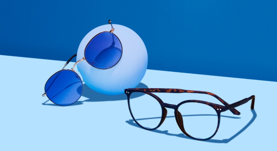 Round blue-lensed sunglasses and tortoiseshell eyeglasses against a gradient blue background.