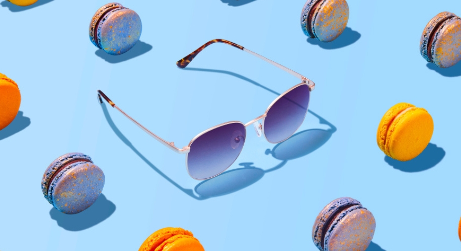 Silver-rimmed sunglasses with blue gradient lenses surrounded by colorful orange and blue macarons.