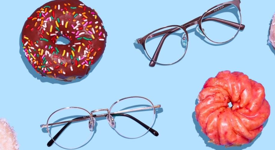 Two pairs of eyeglasses beside donuts with different colorful toppings on a blue background.