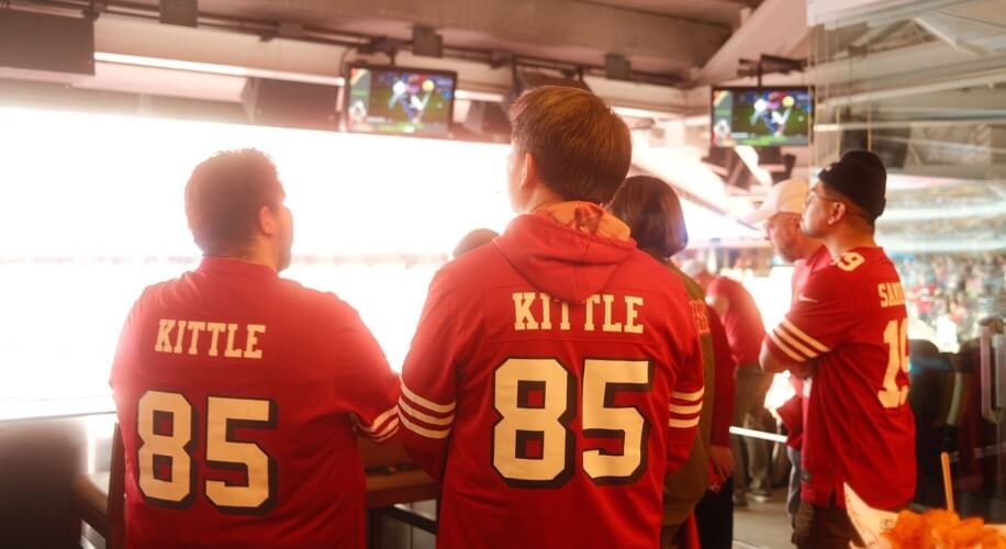 Two people wearing red jerseys with &quot;KITTLE&quot; and number &quot;85&quot; printed on the back.