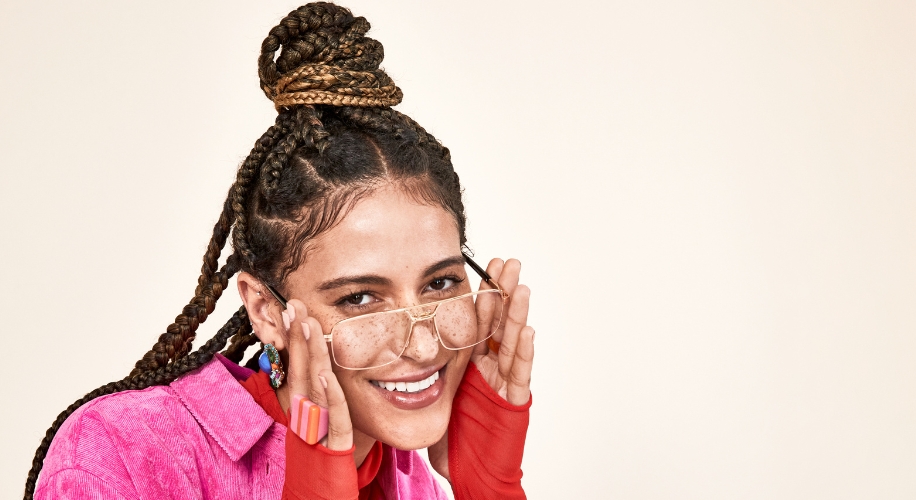 Smiling person wearing oversized clear glasses and a pink shirt with red sleeves.